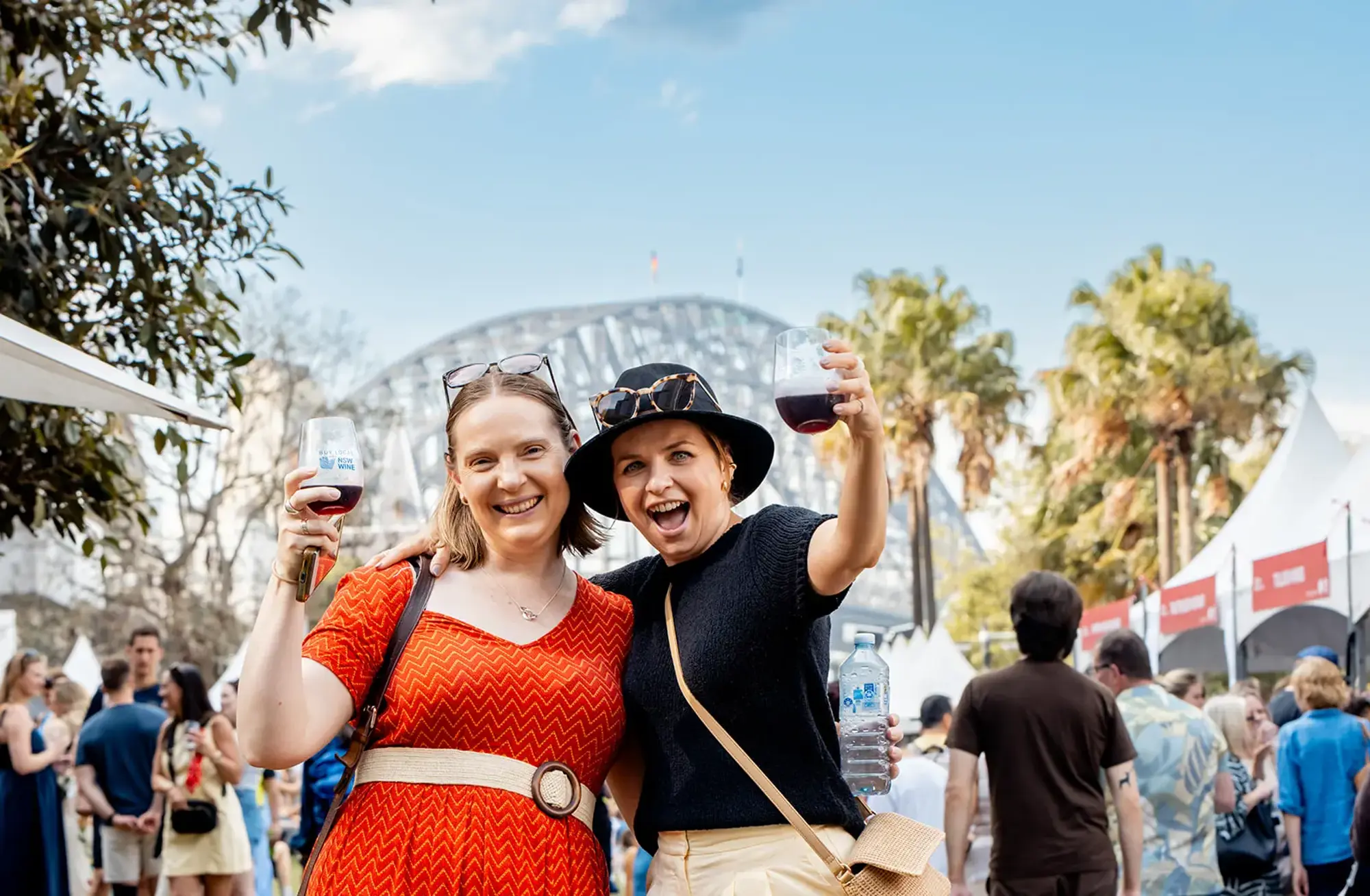 two women holding wine glasses in front of a crowd of people