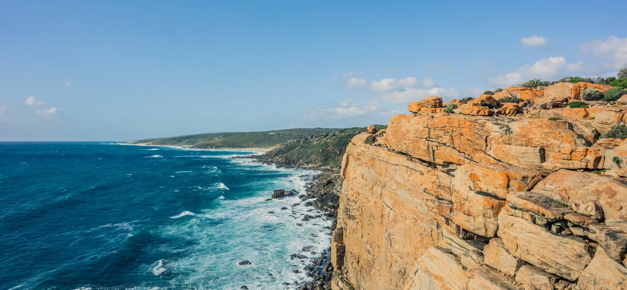 a rocky cliff with a body of water and blue sky