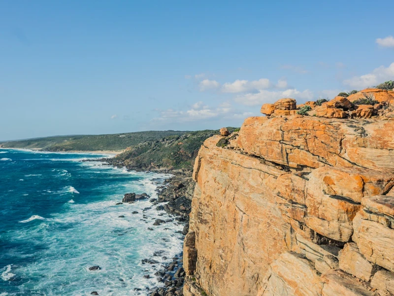 a rocky cliff with a body of water and blue sky