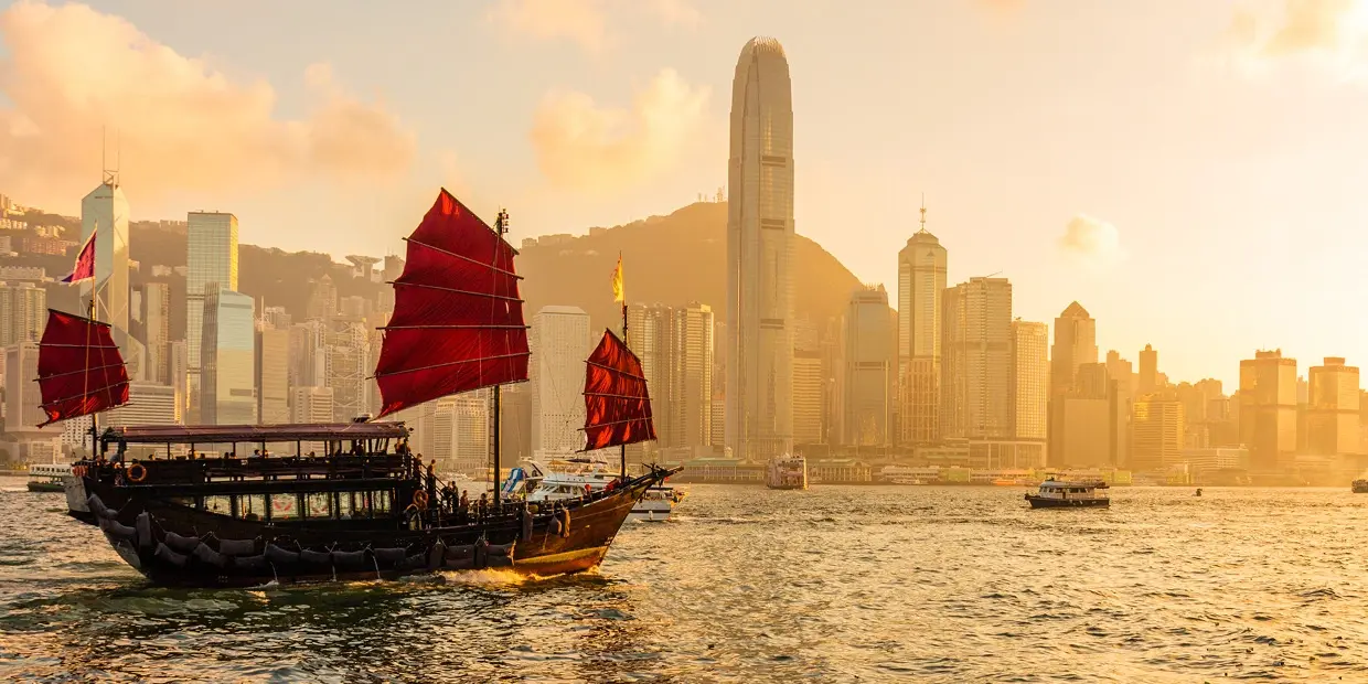 a boat with red sails on water with a city in the background